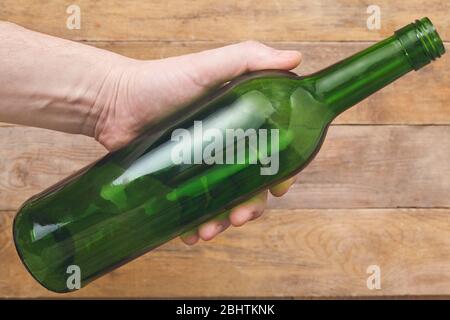 Hand hält eine Weinflasche auf Holzhintergrund. Draufsicht. Stockfoto