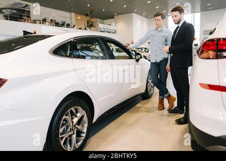 Attraktive Verkäufer trägt Business Anzug zeigt neues Auto interessierten Käufer Stockfoto