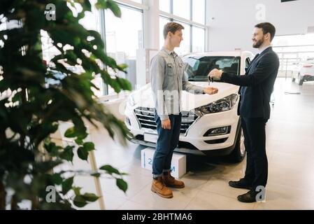 Autoverkäufer Übergabe Schlüssel für neues Auto an junge Mann Käufer in Auto-Händler, vor dem Auto. Stockfoto