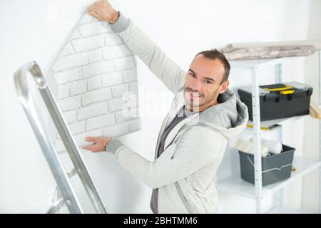 Porträt des Mannes, der Rolle der Tapete in der Wohnung hält Stockfoto