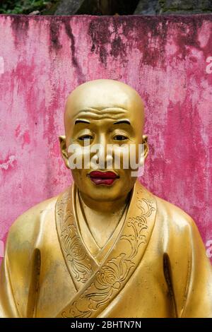 Goldene Statue vor einer rosa Wand - Tempel in der Nähe von Hong Kong - rote Lippen, keine Haare. Teuflich, Tempel der zehntausend Buddhas Stockfoto