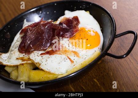 Leckere Eier mit Jabugo Schinken in schwarz Bratpfanne auf hölzernen Tischplatte Stockfoto