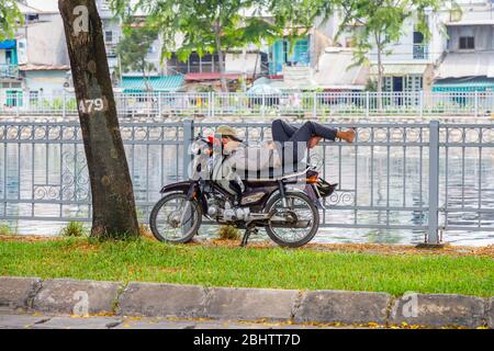 Ein Einheimischer schläft auf seinem Honda Super Dream Motorrad an einem Fluss: Blick auf die Straße in Saigon (Ho Chi Minh Stadt), Südvietnam Stockfoto