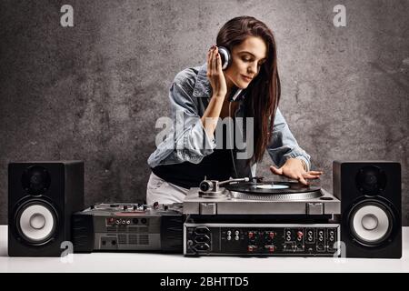DJ-Frau spielt Musik auf einem Plattenteller gegen eine rostige graue Wand Stockfoto