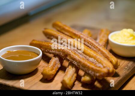 Exquisite Churros mit Zucker und zwei süßen Saucen zu begleiten, auf einem Holztisch bestreut Stockfoto