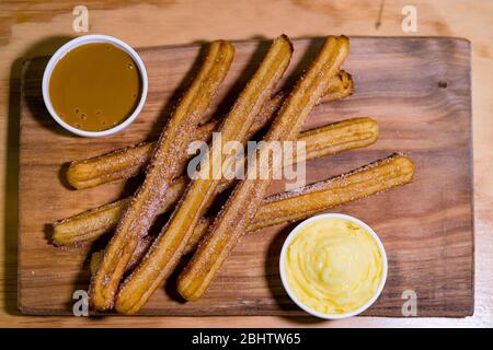 Exquisite Churros mit Zucker und zwei süßen Saucen zu begleiten, auf einem Holztisch bestreut Stockfoto