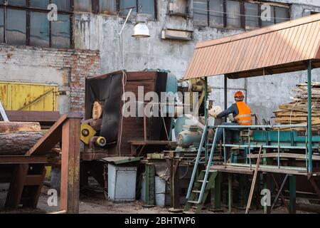 Entfernung der Rinde von den großen Balken auf dem Sägewerk. Die Vorbereitung der hölzernen Balken bis zum Sägen auf der Schnittlinie auf dem Sägewerk. Die Holzindustrie. Ein Haufen von Baumstämmen liegt Stockfoto