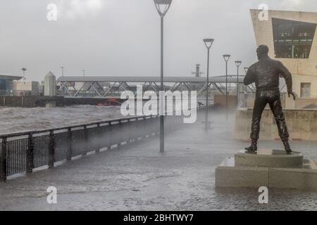 Wellen brechen bei ungewöhnlich hoher Flut über die Promenade am Pier Head in Liverpool, neben dem Mersey Ferries Terminal und der Captain Walker Statue Stockfoto