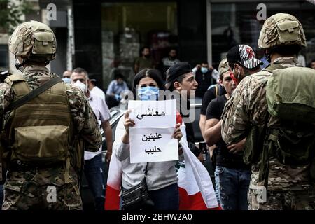 Zouk Mikael, Libanon. April 2020. Ein regierungsfeindlicher Demonstrant hält ein Plakat mit der Aufschrift "Mein Gehalt entspricht dem Preis von zwei Milchdosen", während er zwei libanesischen Soldaten während eines Protestes in Zouk Mikael gegen die hohen Lebenshaltungskosten und die Abwertung der lokalen Währung gegenübersteht. Dutzende Demonstranten versammelten sich und blockierten am Montag wichtige Straßen, um gegen die sich verschlechternde Wirtschaftskrise des Landes zu protestieren und sich einer Sperrung des Coronavirus zu widersetzen. Quelle: Marwan Naamani/dpa/Alamy Live News Stockfoto