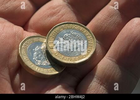 Zwei Bimetallmünzen aus Großbritannien, die in einer Männerhandfläche gehalten und aus nächster Nähe geschossen wurden Stockfoto