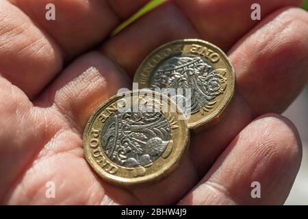 Eine männliche Hand mit zwei britischen (Neu-) Pfund-Münzen, die die Rückseite (Schwänze) zeigen, schoss aus nächster Nähe Stockfoto