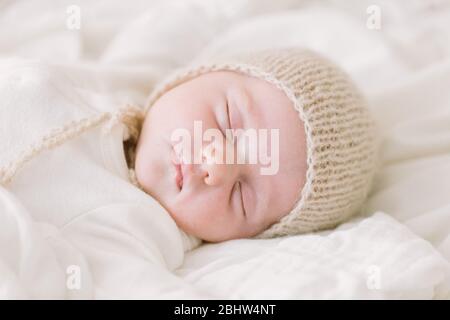 Neugeborenes Baby in Strickhaube schlafen auf weißem Bett Stockfoto