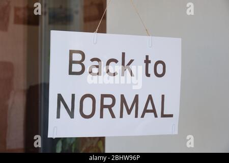 Das Schild "zurück zur normalen", das nach der Sperrung durch Coronavirus (Covid-19) an einem Schaufenster hängt, wird erleichtert. Economy Restart Konzept. Stockfoto