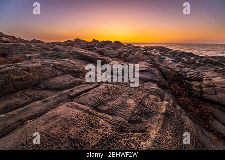 Ein herrlicher Blick auf den Sonnenuntergang über dem Wasser an der chilenischen Küste. Eine idyllische Strandlandschaft mit dem Sonnenlicht, das die Felsen mit Orangentönen beleuchtet Stockfoto