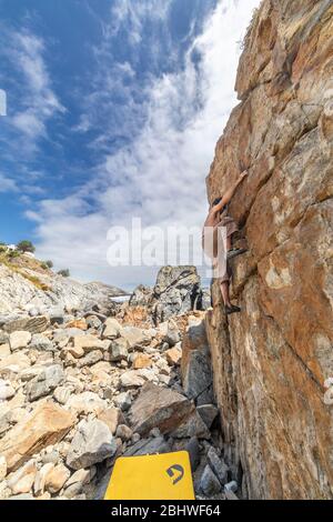 Männlicher Felskletterer beim Bouldern ohne Seil auf einem Boulderbereich vor dem Meer. Ein großer Stein für Menschen mit Beharrlichkeit und Selbstvertrauen Stockfoto