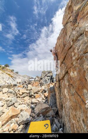 Männlicher Felskletterer beim Bouldern ohne Seil auf einem Boulderbereich vor dem Meer. Ein großer Stein für Menschen mit Beharrlichkeit und Selbstvertrauen Stockfoto