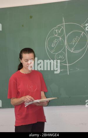 Neben der Schule steht ein Mädchen in einem roten T-Shirt und hält Papiere in den Händen Stockfoto