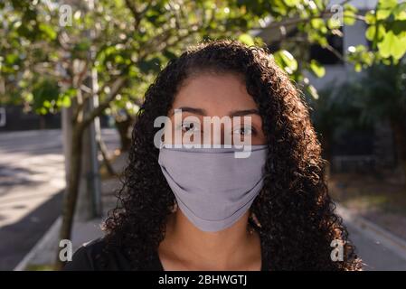 Schwarze Frau auf urbanem Hintergrund in Freizeitkleidung mit einer medizinischen Gesichtsmaske Stockfoto