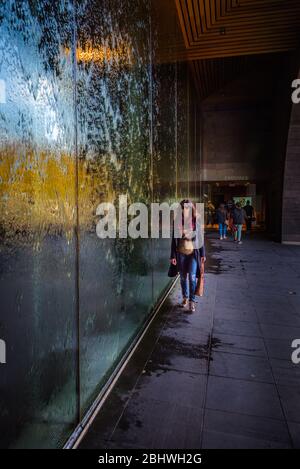 Eine Besucherin spaziert am gläsernen Wasservorhang des Melbourne Arts Museum in Australien entlang. Stockfoto