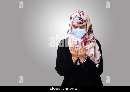 Muslimische Frau mit medizinischer Maske schützen Infektion von Coronavirus (covid-19) beten allah. Isoliert grauen Hintergrund. Stockfoto