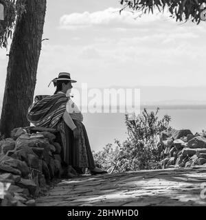 Schwarz-Weiß-Fotografie einer peruanischen indigenen Quechua-Frau, die sich auf der Taquile-Insel, dem Titicaca-See, Peru, an einer Mauer ausruht. Stockfoto