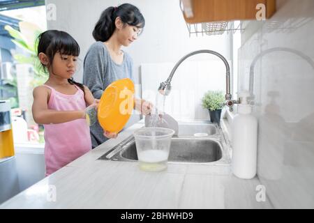 Glückliche Mutter und Tochter waschen Geschirr mit Waschmittel in der Küche Stockfoto