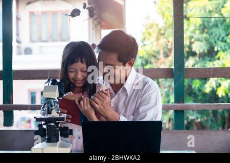 Coronavirus oder 2019 -nCoV Ausbruch Schulabschaltungen. Vater und Tochter lächeln und lernen von zu Hause aus mit Laptop und Mikroskop Stockfoto