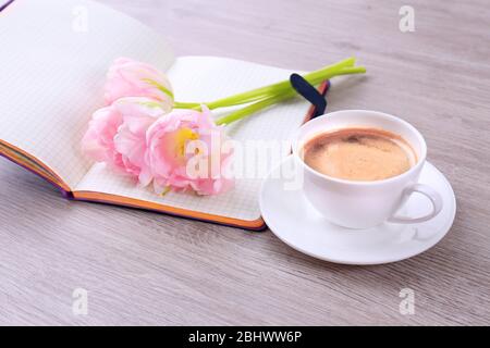 Schöne Tulpen mit Tagebuch und Tasse Kaffee auf Holzhintergrund Stockfoto