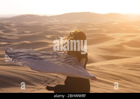Ein Mädchen mit langen Haaren in einem schwarzen Kleid läuft in der Wüste in das Sonnenlicht Stockfoto