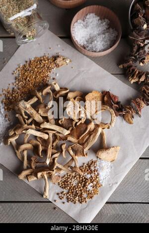 Getrocknete Pilze mit Gewürzen auf Papier auf Holztisch, Draufsicht Stockfoto