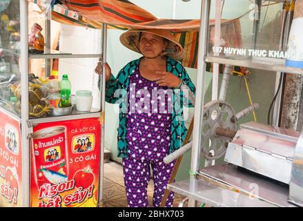 Can Tho Vietnam - Oktober 15 2013; Frau in lila und türkis gekleidet tragene traditionelle konische Hut steht an ihrem Straße Verkaufsschrank in der City str Stockfoto