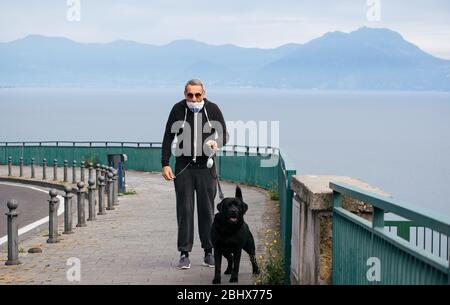 Neapel, Italien. April 2020. Ein Mann, der eine Gesichtsmaske als vorbeugende Maßnahme trägt, geht mit seinem Hund während der SperrungNach der COVD19-Pandemie, die Italien stark getroffen hat, hat der Premierminister Giuseppe Conte strenge Beschränkungen für die Quarantäne angeordnet, um die Ausbreitung des Corona-Virus zu minimieren. Quelle: SOPA Images Limited/Alamy Live News Stockfoto