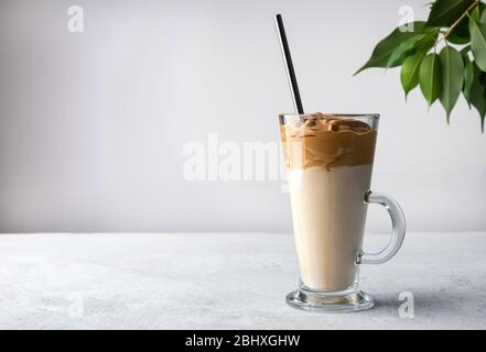 Hohe Glasbecher mit koreanischem Dalgona-Kaffee auf weißem Hintergrund mit grünen Blättern. Kopierbereich Stockfoto