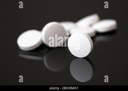 Weiße Pillen werden in dunklem Glas reflektiert, Tabletten auf schwarzem Hintergrund. Konzept der Apotheke, Medikamente oder Vitamine Stockfoto