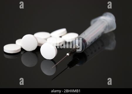 Weiße Pillen und Spritze auf dunklem Glas, Tabletten auf schwarzem Hintergrund. Konzept der Injektion von Medikamenten oder Vitaminen Stockfoto