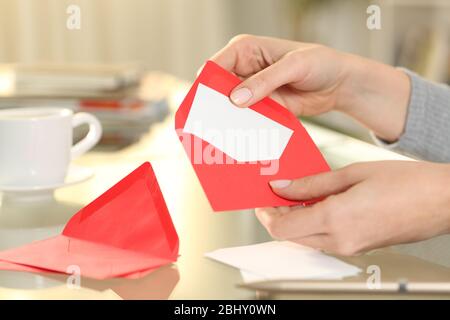 Nahaufnahme der Frau Hand setzen Gruß Dankeskarte auf einem roten Umschlag sitzen auf einem Schreibtisch zu Hause Stockfoto