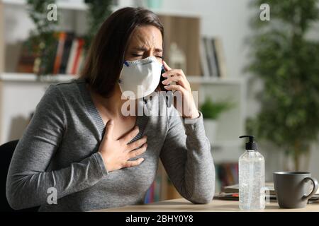 Frau mit Schmerzen mit Coronavirus Symptome tragen Schutzmaske Anruf auf dem Smartphone zu Hause Stockfoto