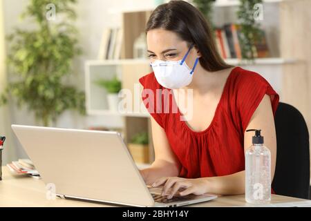 Glückliche Frau mit Schutzmaske Maske due Coronavirus Eingabe auf Laptop sitzen auf einem Schreibtisch zu Hause Stockfoto