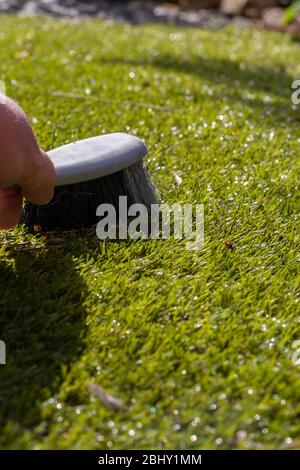 Mann putzt Müll auf Kunstrasen mit einem Handpinsel in der Sonne. Gartenarbeit Konzept Stockfoto