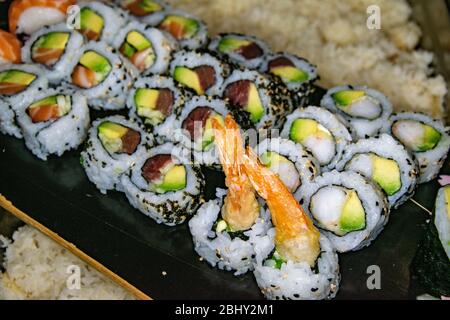 Eine abwechslungsreiche Auswahl an frisch zubereiteten kalifornischen Sushi-Rollen, die auf einem Skateboard präsentiert werden Stockfoto