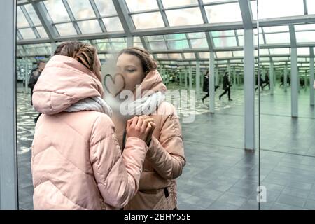 Teen Mädchen zieht ein Herz auf einem Spiegel mit vielen Reflexionen, Rekursion. Das Thema der Einsamkeit in der Großstadt Stockfoto