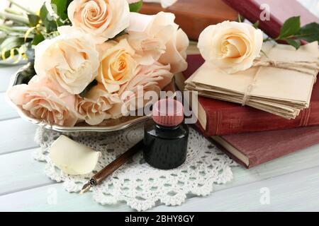 Frische Rosen mit altem Buch und Buchstaben auf farbigem Holztisch Hintergrund. Vintage-Konzept Stockfoto