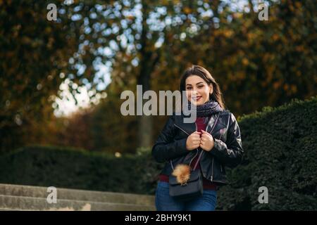 Stylische schöne Dame in einer schwarzen Lederjacke mit schwarzer Tasche und burgunderfarbener Bluse. Attraktive junge Frau lächeln Stockfoto