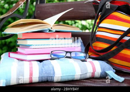 Bücher, Gläser und Tasche auf der Bank im Freien Stockfoto