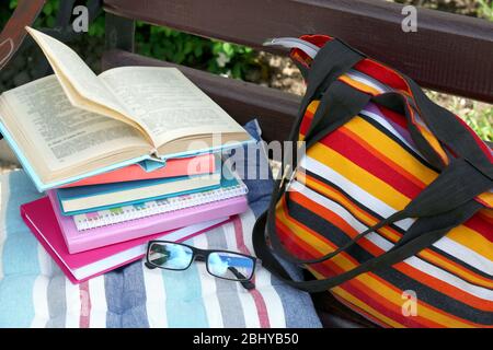 Bücher, Gläser und Tasche auf der Bank im Freien Stockfoto