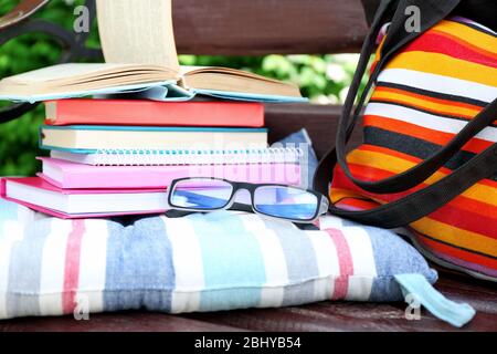 Bücher, Gläser und Tasche auf der Bank im Freien Stockfoto