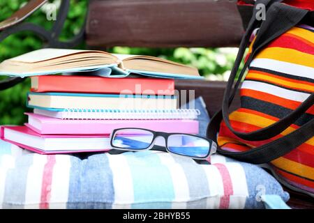 Bücher, Gläser und Tasche auf der Bank im Freien Stockfoto