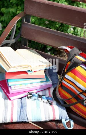 Bücher, Gläser und Tasche auf der Bank im Freien Stockfoto