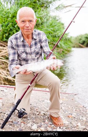 Portrait von zufriedenen Jahren Fischer mit frischen Forellen am Flußufer auf Sommer Stockfoto