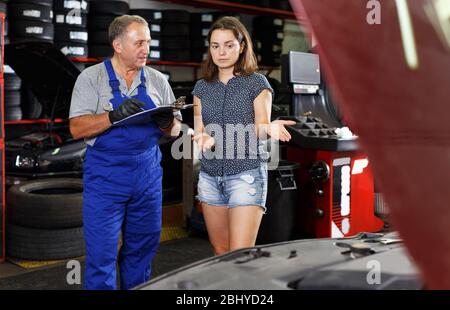 Älterer Mann Auto Mechaniker in der Werkstatt stehen mit weiblichen Kunden, Schreiben Arbeitsblatt für Reparaturen des Fahrzeugs Stockfoto